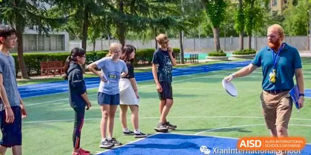 A group of Xi'an International School students standing and chatting on an outdoor sports court in casual athletic wear.
