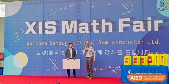 Two adults presenting on a stage during the Xi'an International School Math (China) Seminar under a blue banner.