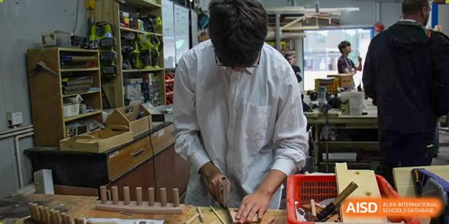 A close-up of a Xi'an International School student wearing a white shirt working on a hands-on project or craftsmanship using wood blocks.