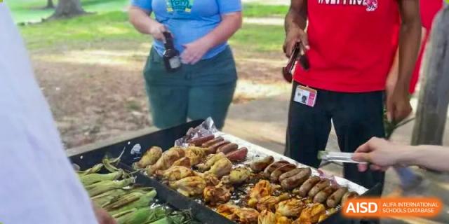 A close-up of a variety of grilled meats and sausages cooking on a barbecue grill at a Xi'an International School outdoor event.