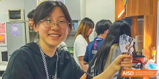 A close-up of a smiling female Xi'an International School student with glasses and her classmates in the background.
