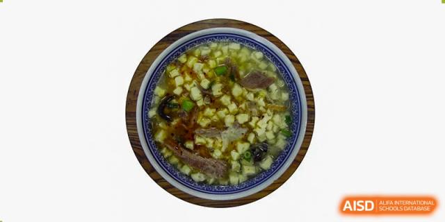 A bowl of traditional Asian food, possibly soup or stew with meat and vegetables, served at Xi'an International School.