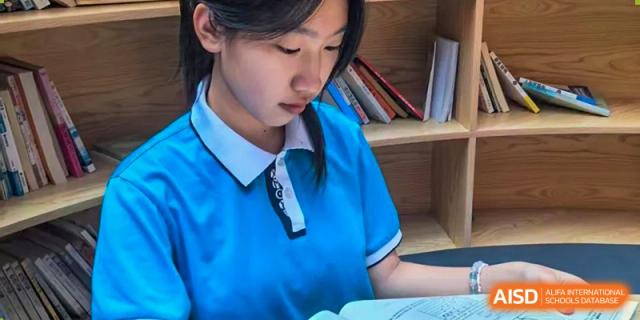 A female student from Xiamen Yingcai school reading a book in a classroom.