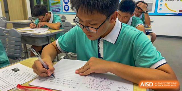 A student from Xiamen Yingcai school writing on paper at a desk.