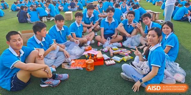A group of Xiamen Yingcai school students enjoying snacks on the grass during an outdoor event.