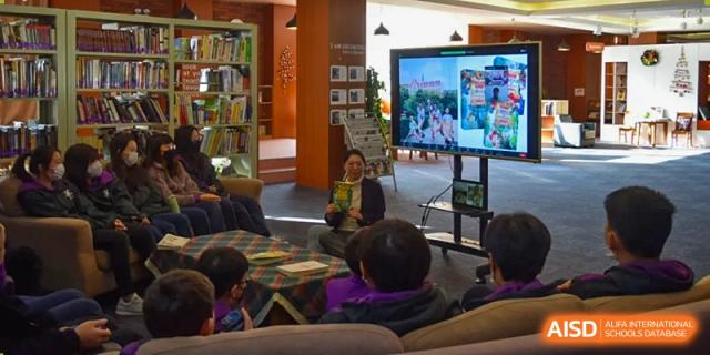 Young students from Yantai Huasheng International School (YHIS) sitting on the floor watching a presentation on a large screen during an activity.