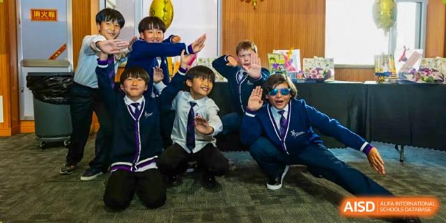 A group of young boys from Yantai Huasheng International School (YHIS) wearing school uniforms, laughing and excitedly waving at the camera.