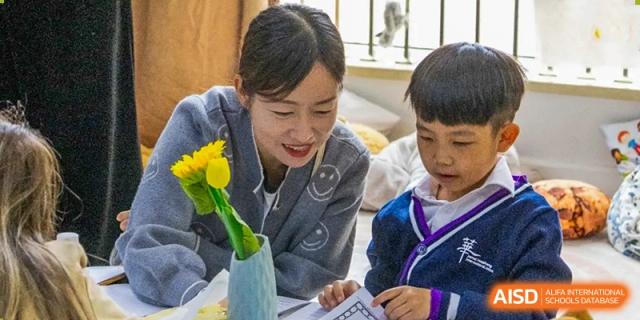 A teacher from Yantai Huasheng International School (YHIS) smiling warmly as she works with a young student on an assignment.