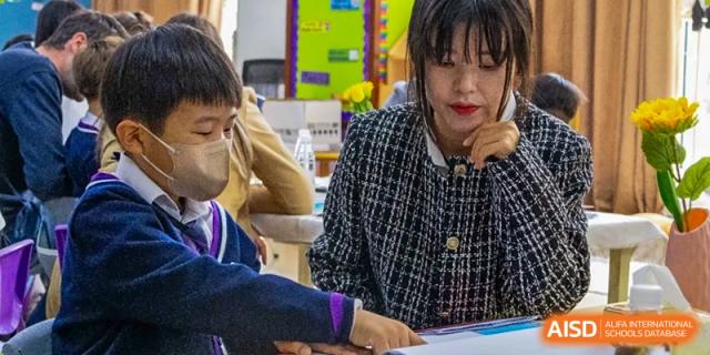 A close-up of a teacher from Yantai Huasheng International School (YHIS) assisting a student at a desk in a classroom.