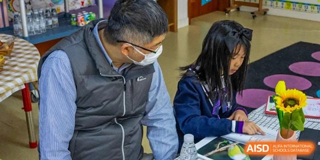 A masked adult from Yantai Huasheng International School (YHIS) talking with a student in a casual setting.