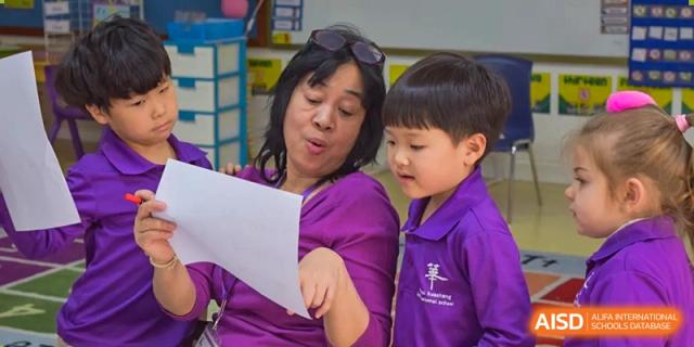 A female teacher or staff member from Yantai Huasheng International School (YHIS) reading a paper with a young student in a purple uniform.