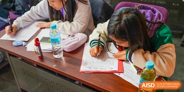 A student from Yantai Huasheng International School (YHIS) intensely focused on writing or completing an assignment at a desk.
