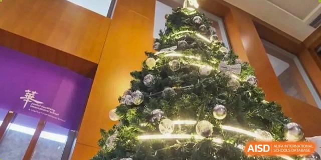 A close-up shot of a brightly lit and decorated Christmas tree with ornaments, likely located within the Yantai Huasheng International School (YHIS).