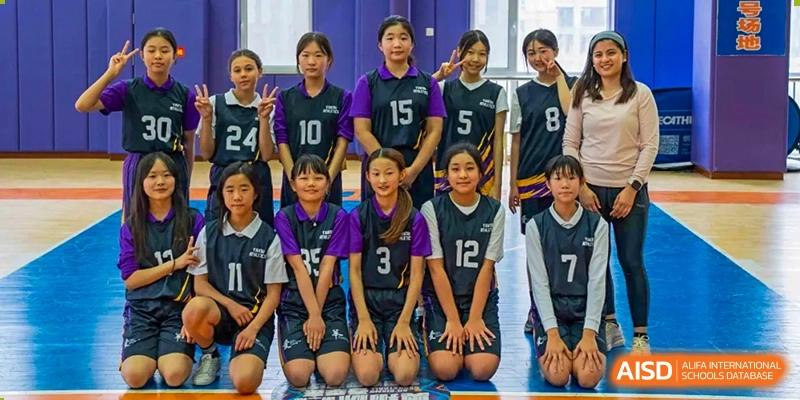 The Yantai Huasheng International School (YHIS) girls' basketball team posing together for a group photo in their black and purple uniforms.
