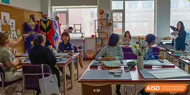 Students from Yantai Huasheng International School (YHIS) studying or working at desks in a classroom setting with shelves and displays in the background.
