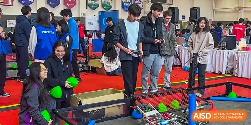 Students from Yantai Huasheng International School (YHIS) participating in a robotics competition or technical challenge, gathered around a large robot on a red and blue mat.