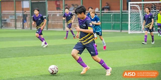 A soccer player from Yantai Huasheng International School (YHIS) dribbling the ball across the pitch during a match.