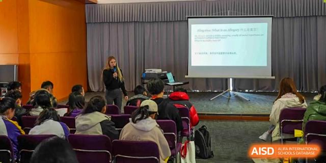 A teacher presenting a lesson or lecture to students seated in an auditorium or classroom at Yantai Huasheng International School (YHIS).