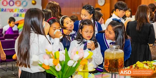 A group of female students from Yantai Huasheng International School (YHIS) smelling or looking at a vase of flowers during an activity.