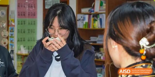 A female student from Yantai Huasheng International School (YHIS) wearing glasses and holding a small object to her face.