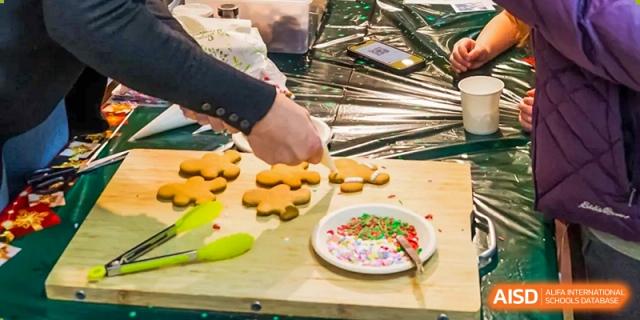 A close-up view of hands decorating gingerbread cookies with colored icing and sprinkles at Yantai Huasheng International School (YHIS).