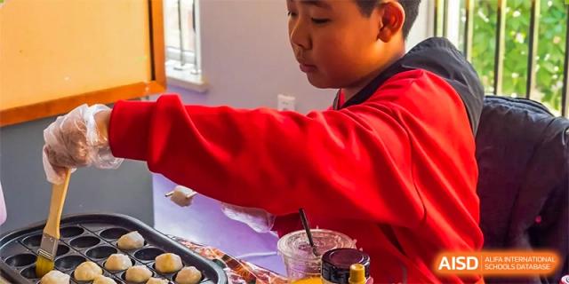 A student from Yantai Huasheng International School (YHIS) in a red shirt concentrating on a craft or food decoration activity.