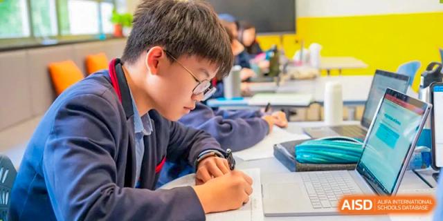 A male student wearing glasses and writing in a notebook during class at Yew Chung International School of Shanghai.