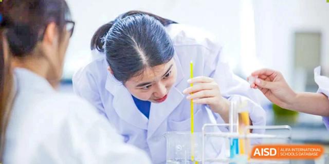A female student in a lab coat using a pipette in a beaker during a science experiment at Yew Chung International School of Shanghai.