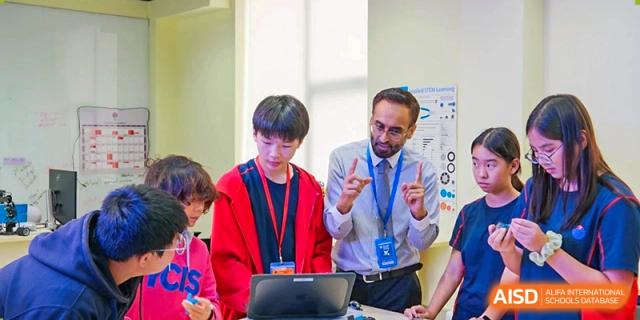 A teacher helping a male student with a laptop in a classroom at Yew Chung International School of Shanghai.