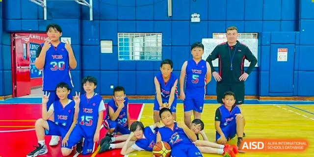 A group of students in basketball uniforms posing for a team photo in a gym at Yew Chung International School of Shanghai.