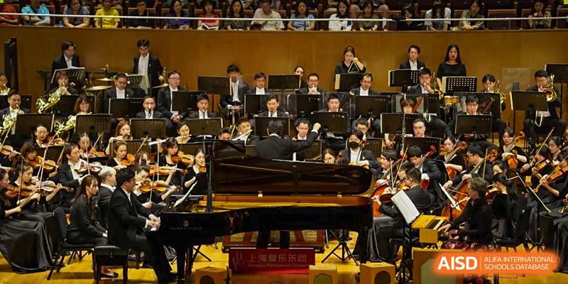 Students performing in an orchestra with a grand piano on a stage at Yew Chung International School of Shanghai.