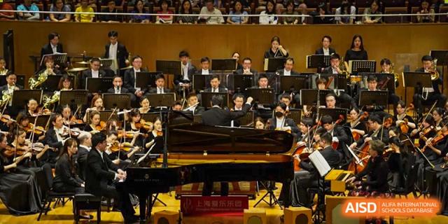 Students performing in an orchestra with a grand piano on a stage at Yew Chung International School of Shanghai.