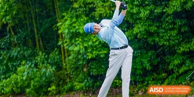 A male student wearing a helmet and swinging a golf club outdoors at Yew Chung International School of Shanghai.