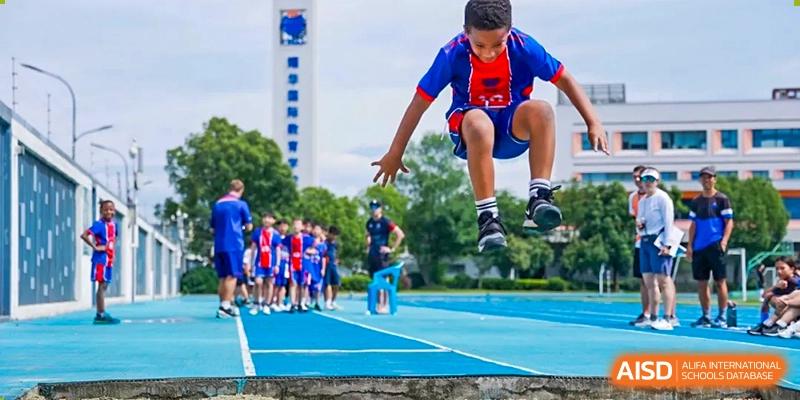 A male student in a red and blue uniform jumping in the air on a running track at Yew Chung International School of Shanghai.