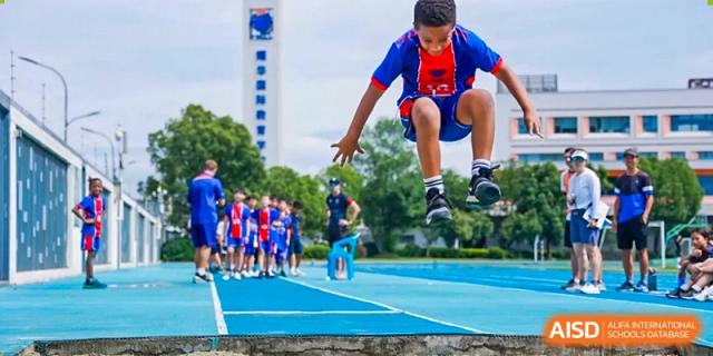 A male student in a red and blue uniform jumping in the air on a running track at Yew Chung International School of Shanghai.