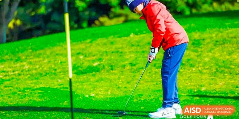 A male student in a red jacket swinging a golf club at Yew Chung International School of Shanghai.