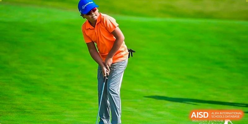 A male student wearing an orange polo shirt and swinging a golf club on a grassy field at Yew Chung International School of Shanghai.