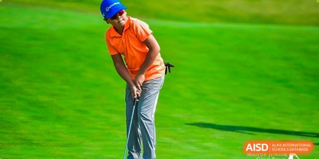 A male student wearing an orange polo shirt and swinging a golf club on a grassy field at Yew Chung International School of Shanghai.