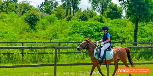 A student on horseback, riding through a grassy area with trees at Yew Chung International School of Shanghai.