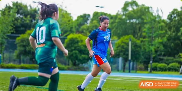 A male student in a green and blue uniform running on a grassy field at Yew Chung International School of Shanghai.