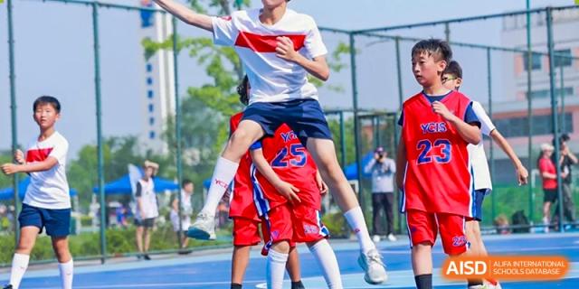 Two students in uniform celebrating a victory on a soccer field, with one student on another's shoulders at Yew Chung International School of Shanghai.