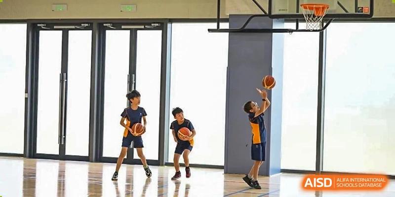 Two students dribbling basketballs in a bright, modern gymnasium with large windows at Yew Wah International Education School of Shanghai Lingang.