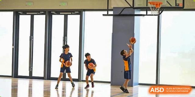 Two students dribbling basketballs in a bright, modern gymnasium with large windows at Yew Wah International Education School of Shanghai Lingang.