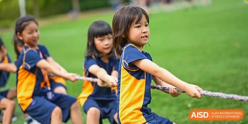 Two young students, a girl and a boy, smiling and pulling a rope during a tug-of-war game at Yew Wah International Education School of Shanghai Lingang.
