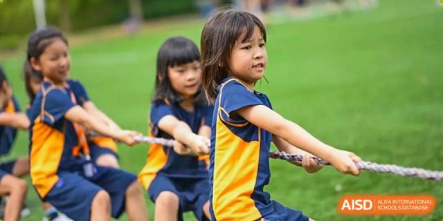 Two young students, a girl and a boy, smiling and pulling a rope during a tug-of-war game at Yew Wah International Education School of Shanghai Lingang.