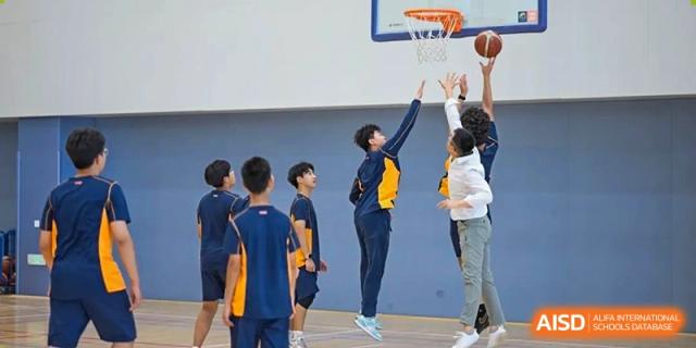 A group of students playing basketball in a gym, with one student jumping to shoot a hoop at Yew Wah International Education School of Shanghai Lingang.