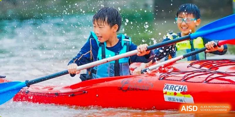 A student wearing a life vest smiles while kayaking on the water, holding a paddle at Yew Wah International Education School of Shanghai Lingang.