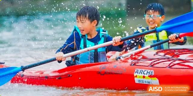 A student wearing a life vest smiles while kayaking on the water, holding a paddle at Yew Wah International Education School of Shanghai Lingang.