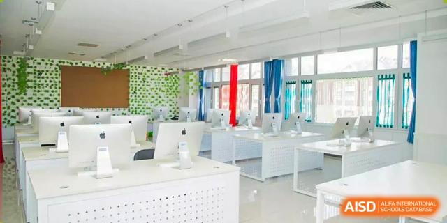 Bright, modern computer lab with rows of white desks and Apple desktop monitors at BIBA (Tianjin International Bilingual Academy).