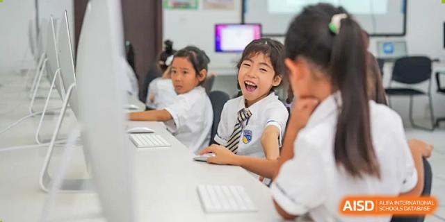 A group of smiling students, one laughing joyfully, participating in a computer lesson at BIBA (Tianjin International Bilingual Academy).